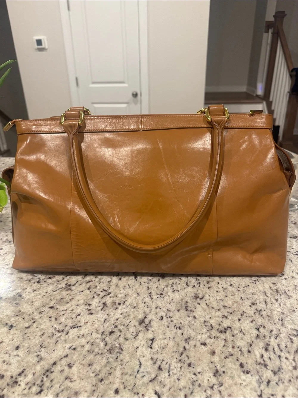 The Find Classic Tan Leather Weekender Travel Bag with Gold Hardware Buckle.